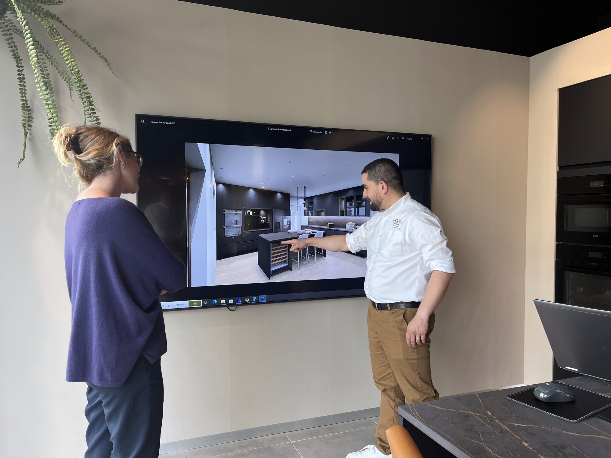 Deux personnes regardent une présentation de cuisine moderne sur un écran mural, avec un plan de travail en marbre au premier plan.