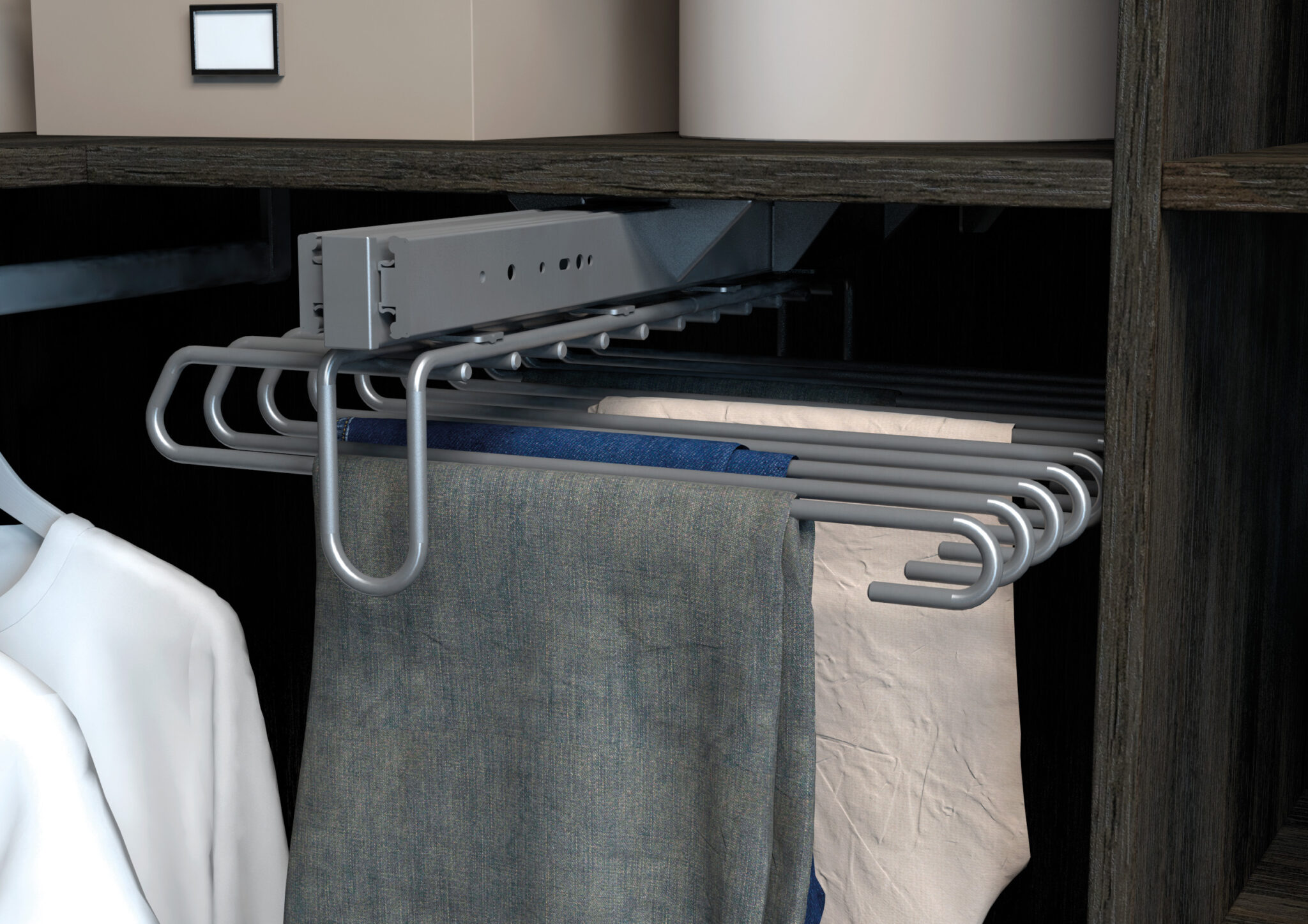 Porte-pantalon coulissant en métal gris avec plusieurs cintres, tenant des tissus bleu, gris et beige dans un placard sombre.