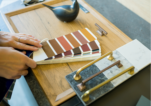 Un nuancier de couleurs est tenu au-dessus d'un plateau en bois, avec des poignées en métal doré et argenté posées à côté.