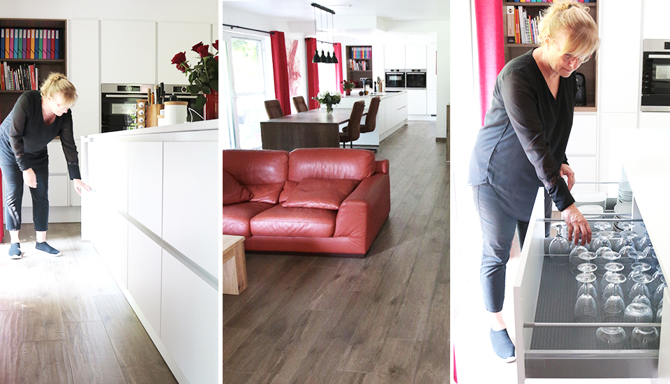 Une femme interagit avec des tiroirs de cuisine blancs, un salon avec canapé rouge et table à manger en arrière-plan.