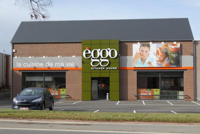 Façade d'un magasin èggo avec logo central, murs en briques, panneaux publicitaires et voiture noire stationnée devant.