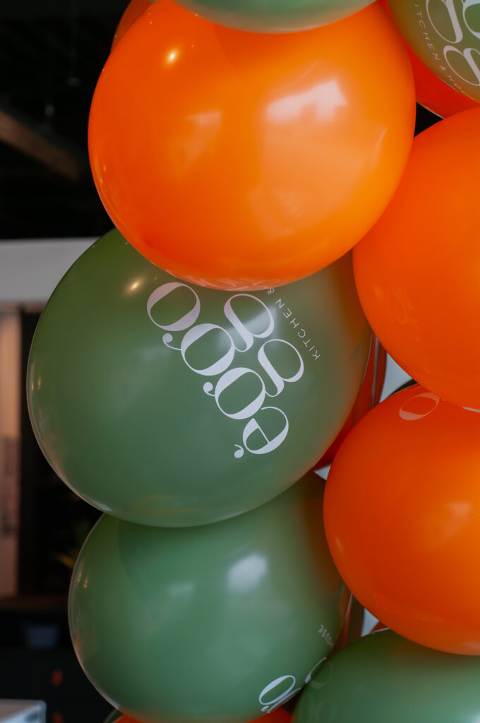 Ballons orange et verts avec le logo èggo imprimé en blanc, disposés en grappes dans un intérieur sombre.