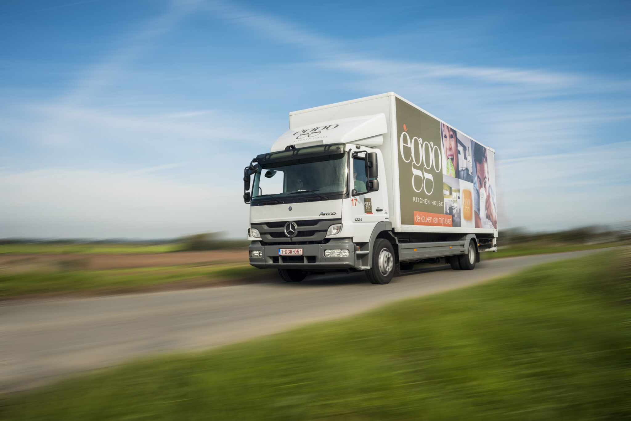 Un camion de livraison blanc avec le logo "èggo" roule sur une route de campagne sous un ciel bleu.