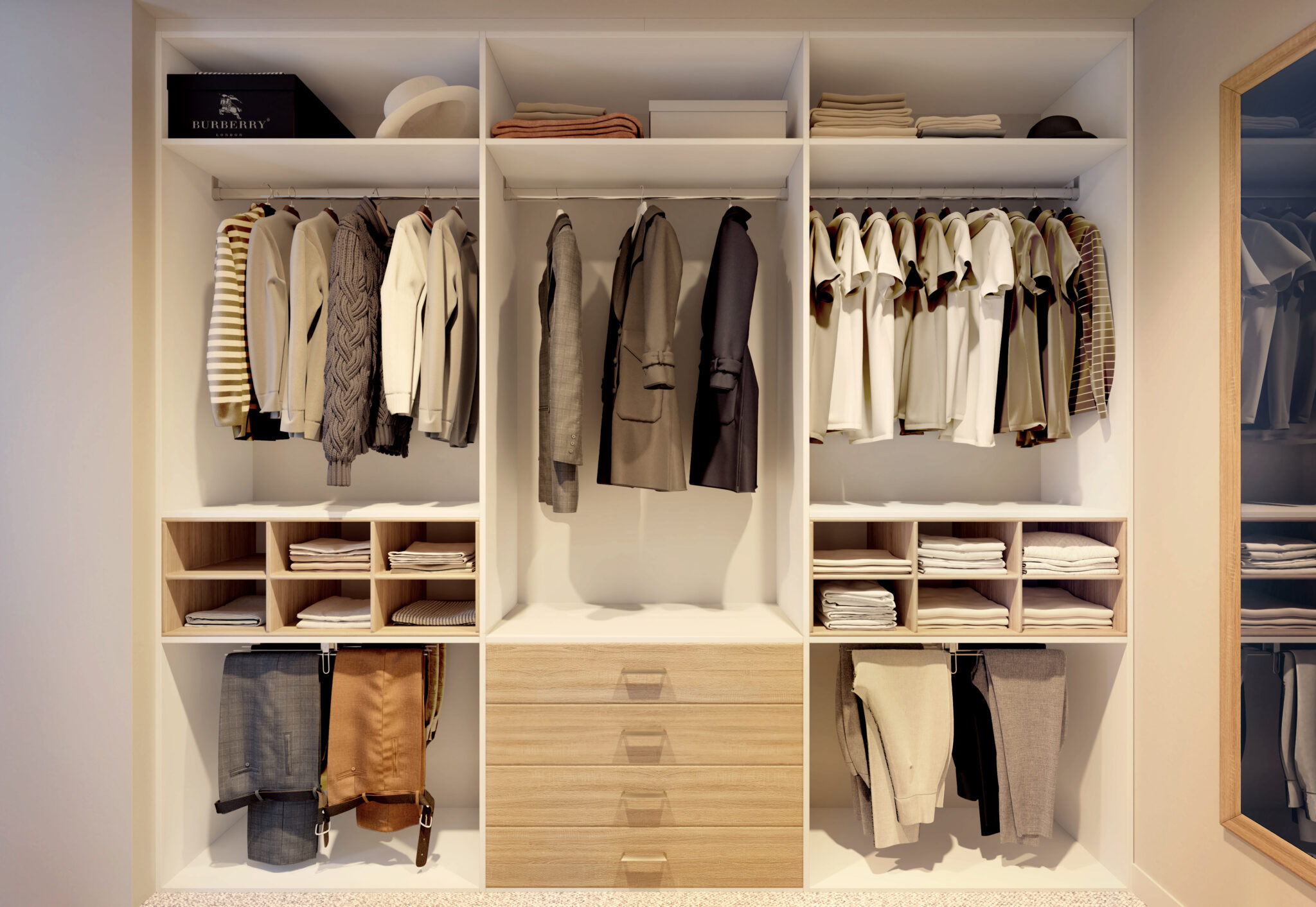 Une garde-robe blanche avec vêtements suspendus, étagères remplies de pulls pliés, et tiroirs en bois clair.