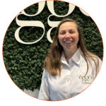 Une femme souriante portant une chemise blanche avec le logo èggo se tient devant un mur végétal avec le logo èggo.