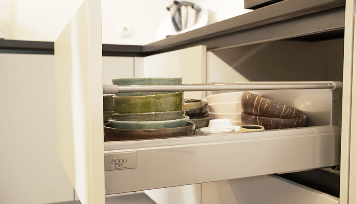 Tiroir de cuisine ouvert avec des assiettes vertes et brunes empilées à côté d'un appareil électroménager blanc.