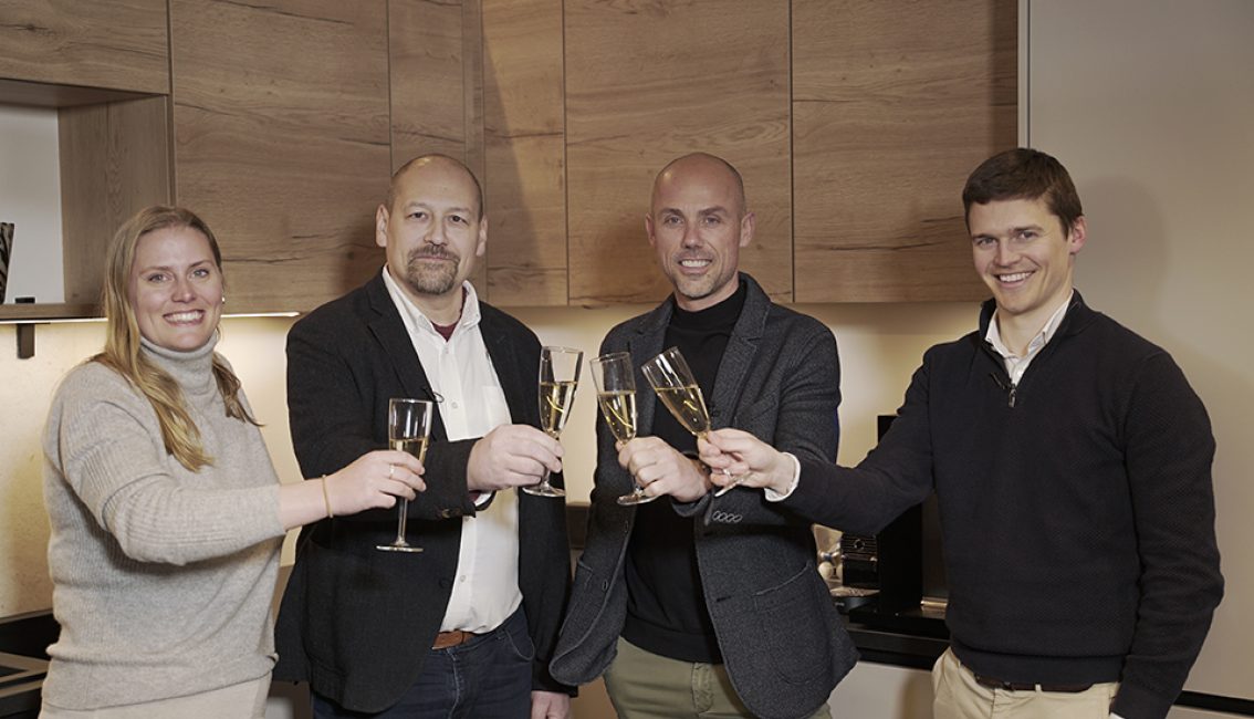 Quatre personnes tenant des flûtes de champagne se tiennent dans une cuisine moderne avec des placards en bois.
